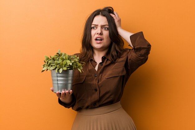 Foto jovem curvilínea plus size mulher segurando uma planta sendo chocada, ela se lembrou de uma reunião importante.