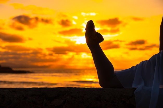 Foto jovem dançarina ao lado da praia ao pôr do sol fazendo spagata com o mar ao fundo