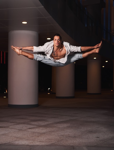 Foto jovem dançarino de balé vestindo camisa branca e calça jeans, pulando em um prédio. dança ao ar livre