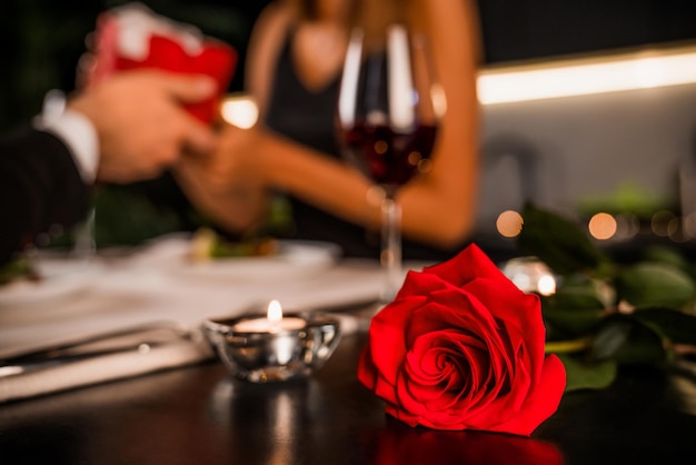 Foto jovem dando a sua namorada caixa de presente para foco presente em rosa e vela em primeiro plano