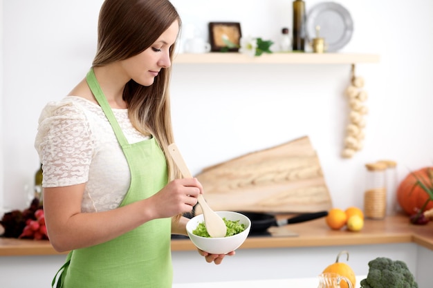 Jovem de avental verde cozinhando na cozinha. Dona de casa misturando salada fresca.