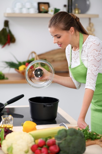 Jovem de avental verde está cozinhando em uma cozinha Dona de casa está provando a sopa com colher de pau