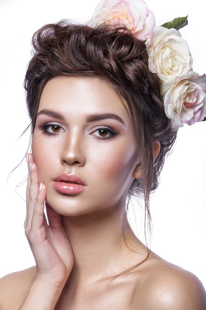 Foto jovem de beleza, pele limpa, bela maquiagem, tranças de penteado e flores rosas no cabelo.