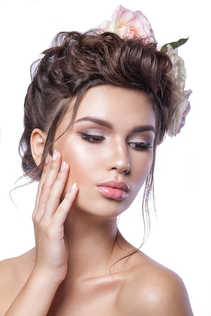 Jovem de beleza, pele limpa, bela maquiagem, tranças de penteado e flores rosas no cabelo.