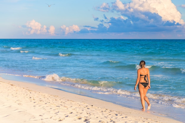 Jovem de biquíni caminhando na praia exótica