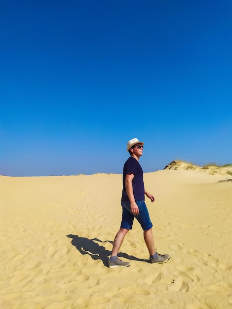 Jovem de blusa branca e shorts marrons andando no deserto