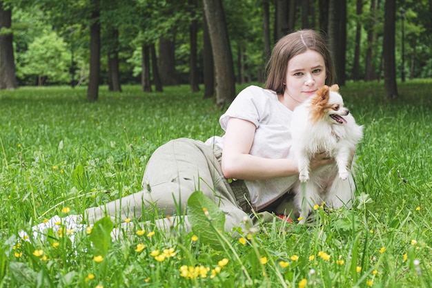 Jovem de cabelo comprido está no gramado do parque com um cachorro Pomeranian