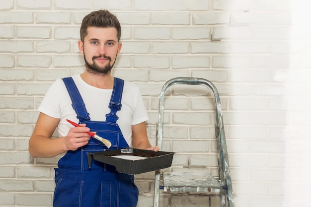 Foto jovem de cabelo escuro está pintando a parede de branco em seu apartamento