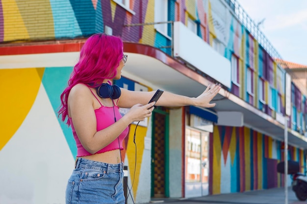 Jovem de cabelo rosa ouvindo música e parando um táxi com a mão