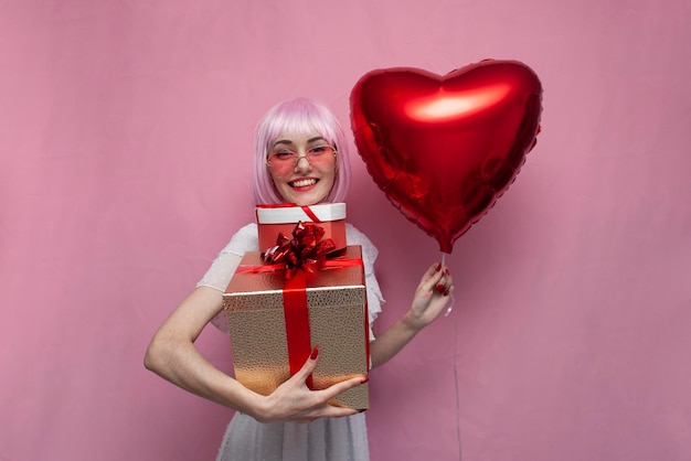 Jovem de cabelo rosa segura balões e presentes e comemora o aniversário de uma mulher com presentes para o Dia dos Namorados