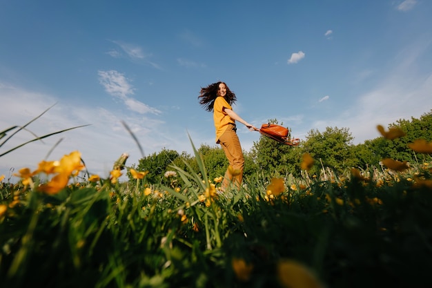 jovem de cabelos escuros corre alegremente em um campo verde com flores amarelas contra um céu azul