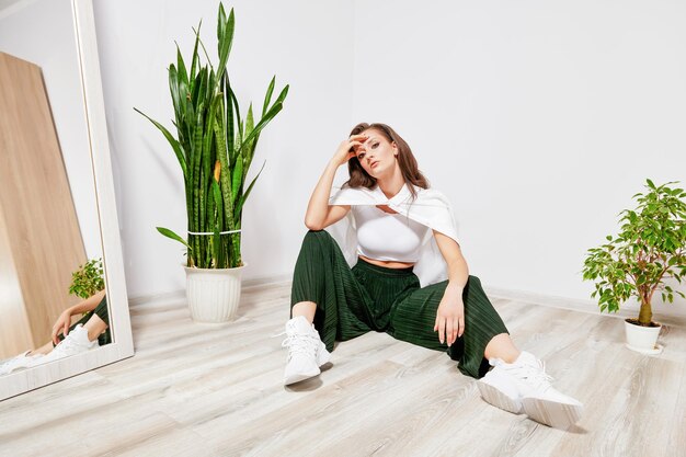 Jovem de calça verde e camisa branca sentada no chão