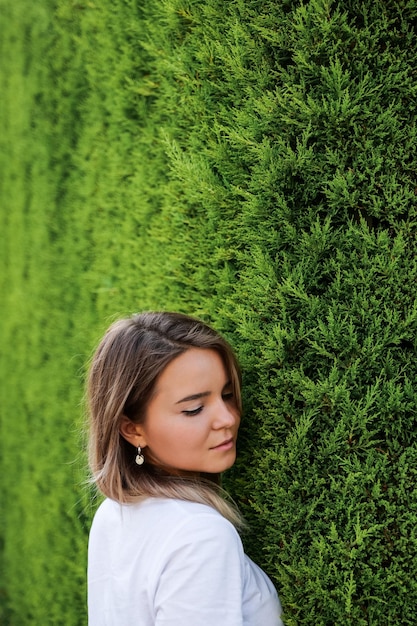 Jovem de camisa branca com maquiagem natural em pé pela cerca verde