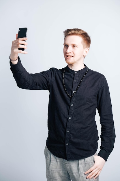 Jovem de camisa preta com um smartphone nas mãos em um fundo branco