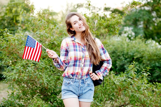 Jovem de camisa xadrez e shorts segurando a bandeira americana