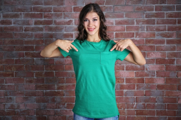 Jovem de camiseta verde em branco em pé contra a parede de tijolos