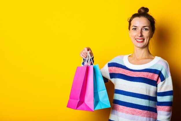 Jovem de camisola segurando sacolas de compras em fundo amarelo.