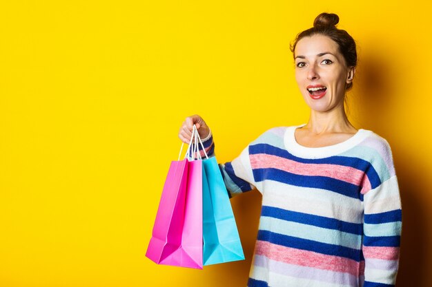 Jovem de camisola segurando sacolas de compras em fundo amarelo.