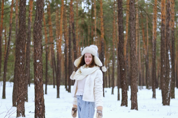 jovem de casaco branco, chapéu quente, luvas andando. parque de inverno gelado. época de Natal