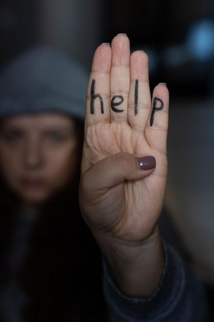 Jovem de chapéu cinza mostrando quatro dedos com inscrição na mão dizendo ajuda Sinal de violência doméstica Abuso psicológico físico mental Vítima de espancamento e sob pressão
