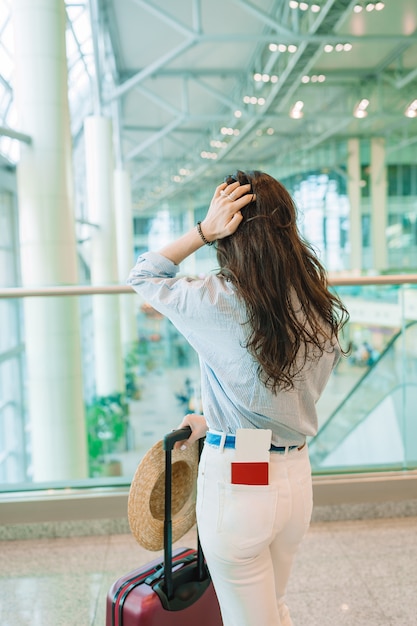 Jovem de chapéu com bagagem no aeroporto internacional, andando com a bagagem dela.