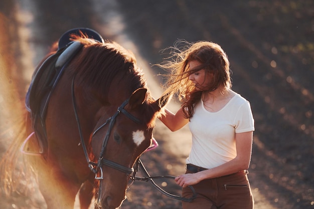 Jovem de chapéu protetor andando com seu cavalo no campo agrícola no dia ensolarado