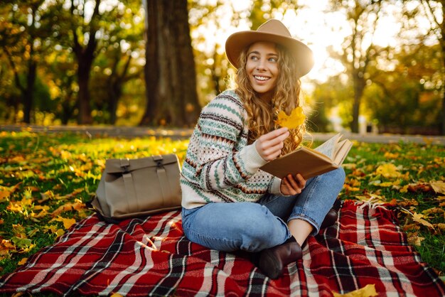 Jovem de chapéu senta-se em uma manta no parque de outono e lê um livro Conceito de educação natural