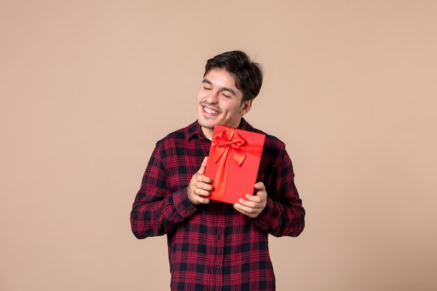 Jovem, de frente, segurando um pacote vermelho com um presente para mulheres na parede marrom