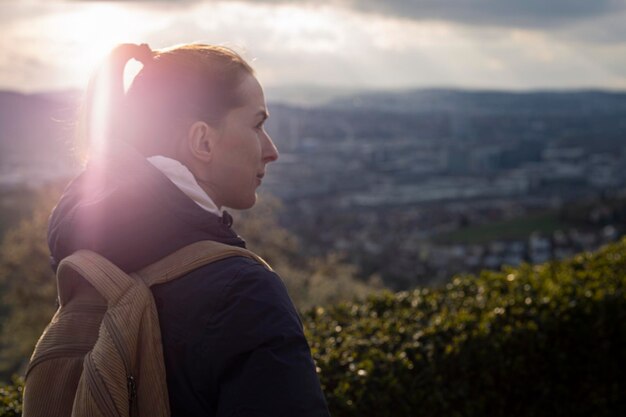 Foto jovem de jaqueta com mochila olha o panorama ao pôr do sol