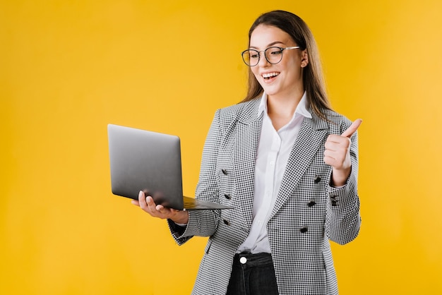 Jovem de jaqueta e camisa usando óculos usando um laptop em fundo amarelo