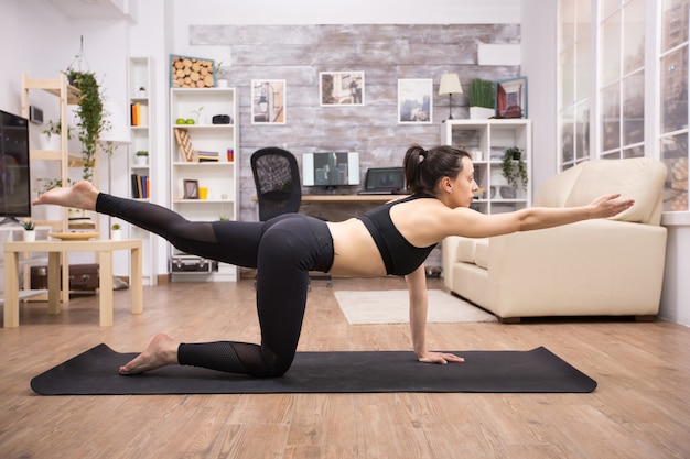 Jovem de legging fazendo pose de ioga de equilíbrio na sala de estar.