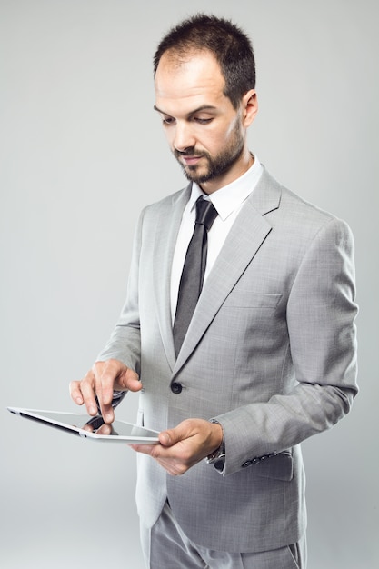 Jovem de negócios usando seu tablet digital sobre fundo cinza.