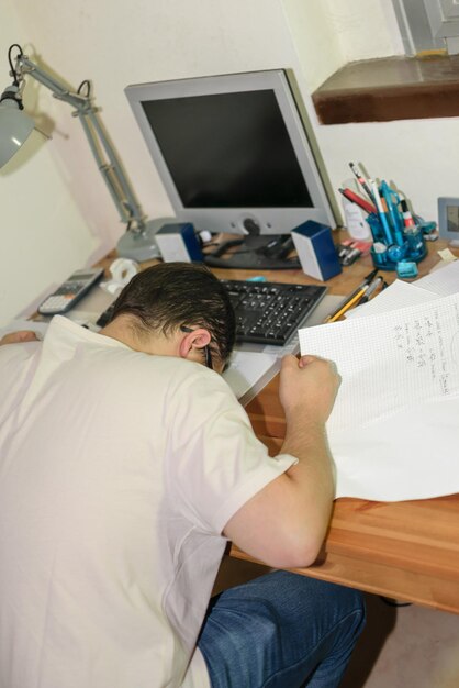 Jovem de óculos com a cabeça na mesa em cima de papéis estressados por seus estudos