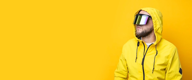 Jovem de óculos de realidade virtual em uma jaqueta amarela desvia o olhar em um fundo amarelo Banner