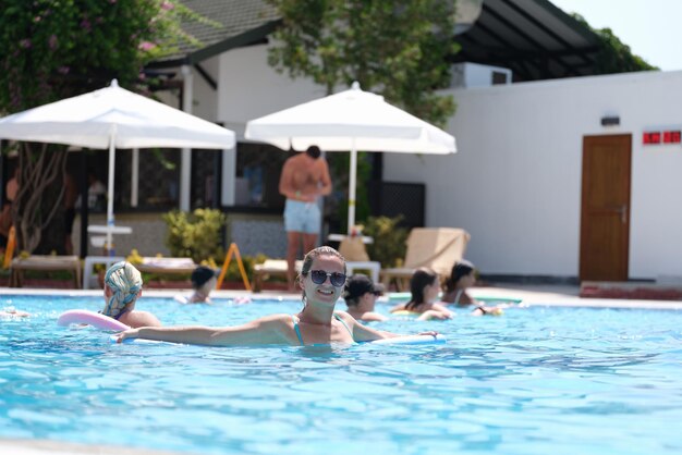 Jovem de óculos de sol nada com macarrão aqua na piscina