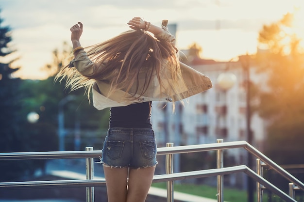 Jovem de óculos de sol se diverte com o pôr do sol ao ar livre ao fundo