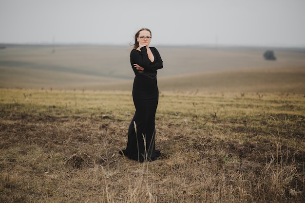 Jovem de óculos e vestido preto posando em um campo