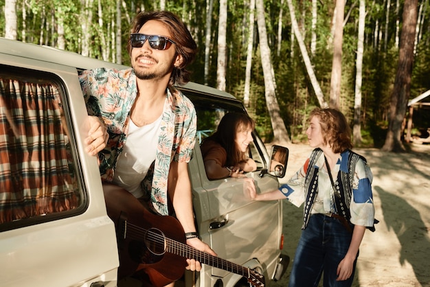 Jovem de óculos escuros com guitarra viajando com seus amigos na floresta