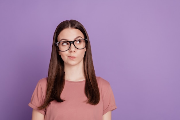 Jovem de óculos pensando isolada em um fundo roxo