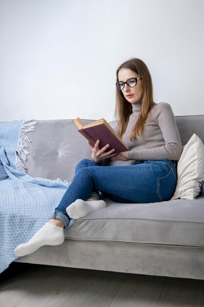 Jovem de óculos sentado em um sofá lendo um livro