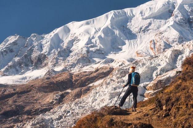 Jovem de pé com mochila no pico da montanha e olhando belas montanhas e geleiras ao pôr do sol