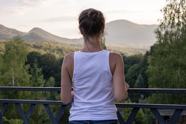 Jovem de pé de costas apreciando a bela paisagem natural com vista para a montanha