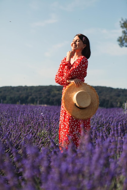 Jovem de pé em um campo de lavanda e segurando um chapéu de palha