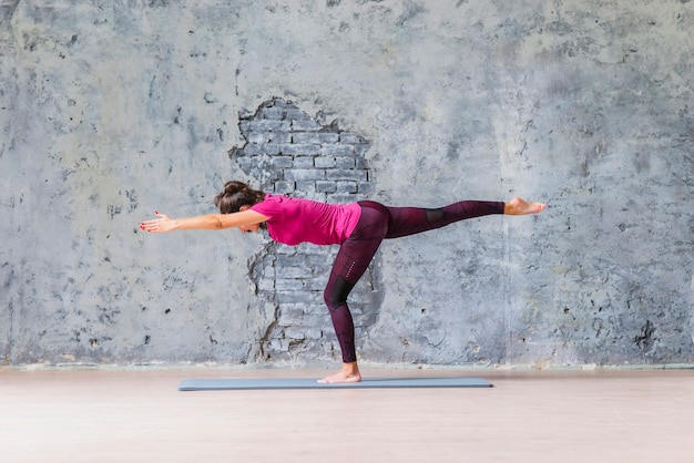 Foto jovem de pé em uma perna fazendo exercícios de fitness contra a parede cinza