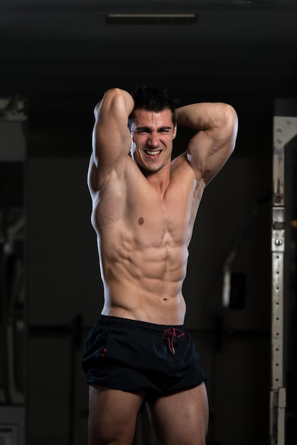 Jovem de pé forte na academia e flexionando os músculos Muscular Atlético Bodybuilder Fitness Modelo Posando Após Exercícios