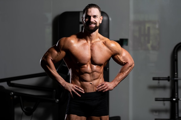 Jovem de pé forte na academia e flexionando os músculos muscular atlético bodybuilder fitness modelo posando após exercícios