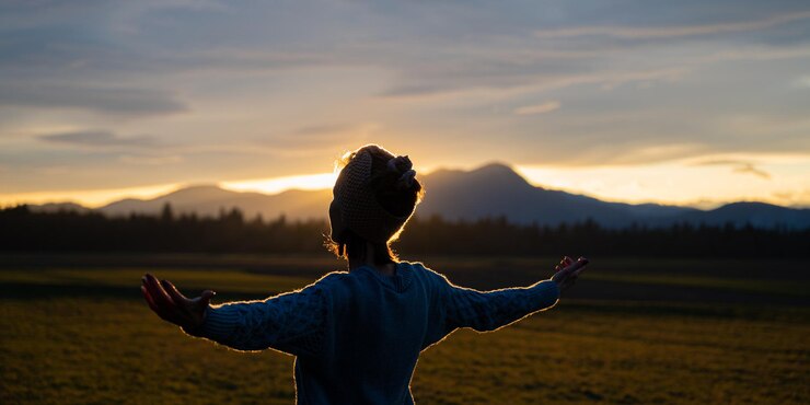 Foto jovem de pé na bela natureza ao pôr do sol meditando com os braços abertos suavemente iluminados pelo sol poente.
