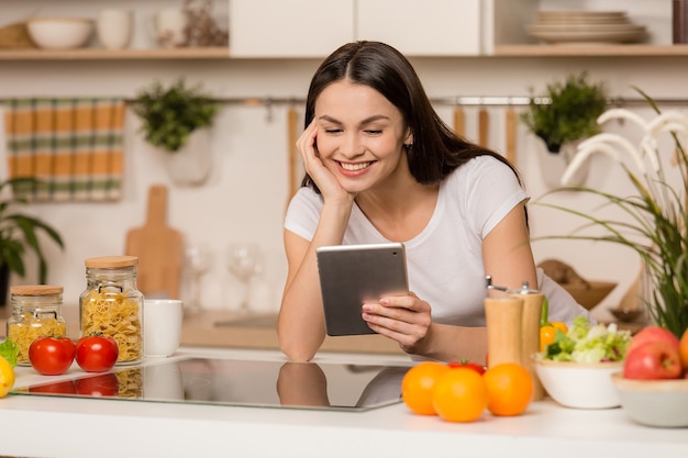 Jovem de pé na cozinha com um tablet