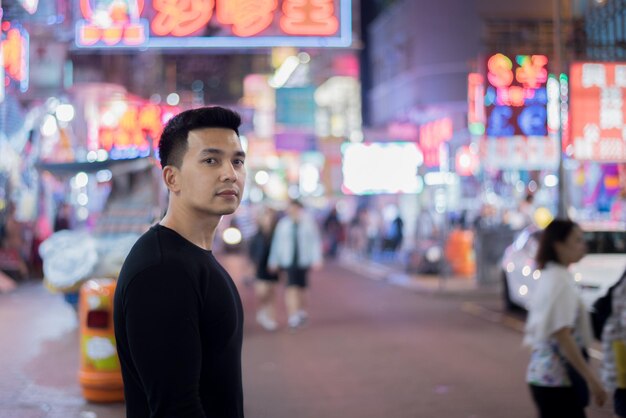 Jovem de pé na rua iluminada da cidade à noite