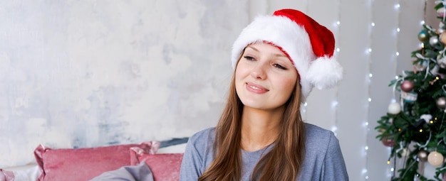 Jovem de pijama azul e chapéu de papai noel no interior do quarto decorado